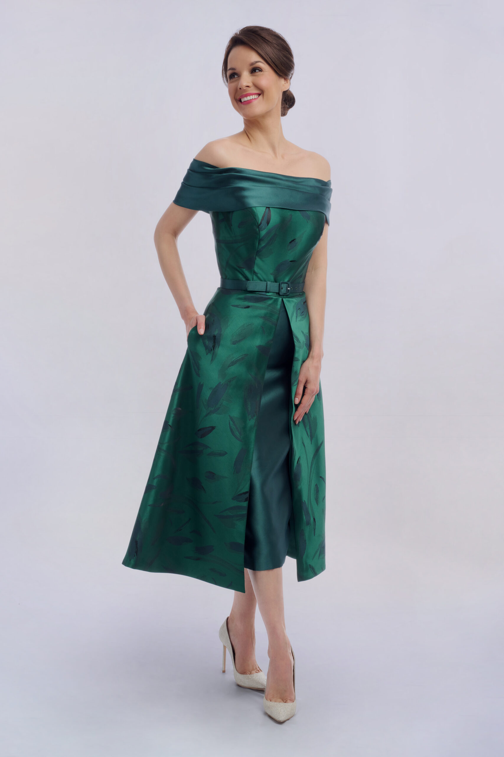 Model in the Holborn emerald green occasion dress with satin bardot neckline, belted waist and split A-line skirt