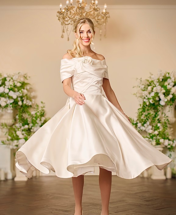 Front view of the Pearl ivory satin tea-length wedding dress with an off-the-shoulder folded neckline, rosette detail at the shoulder, ruched bodice and a full circle skirt.